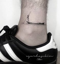 a small tattoo on the ankle of a man who is standing in a boat and fishing