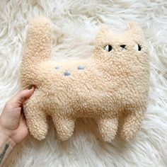 a hand holding a stuffed animal on top of a white rug with blue eyes and nose