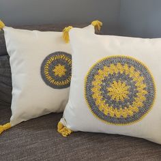 two white pillows with yellow tassels are on a gray couch next to each other