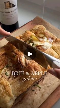 a person cutting food on top of a wooden cutting board next to a bottle of wine