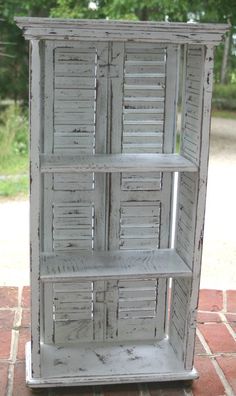 an old white bookcase with shutters on the top and bottom, sitting on a brick floor