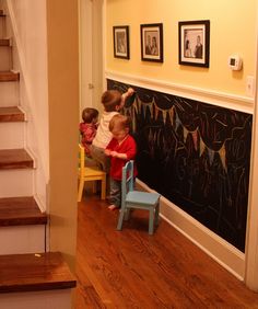 two children are playing with chairs in front of a chalkboard on the wall behind them