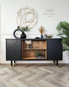 a black and wood sideboard with two plants on top, one plant is in the corner