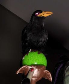 a black bird sitting on top of a green ball with a brown head and beak