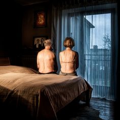 two people sitting on a bed looking out the window