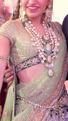 a woman in a green and gold sari with jewelry on her head, smiling at the camera