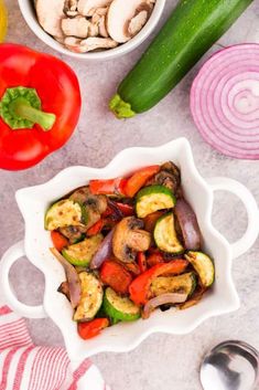 a white bowl filled with vegetables next to some sliced up tomatoes and cucumbers