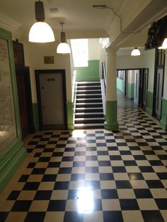 an empty hallway with black and white checkered flooring, green doors and stairs