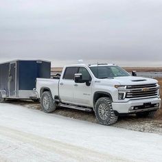 a white truck pulling a trailer on a snowy road