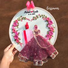 a person holding up a hand embroidered ornament with a pink dress on it