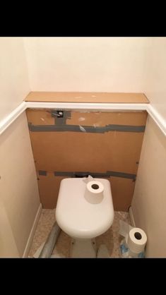 a white toilet sitting inside of a bathroom next to a roll of toilet paper on the floor