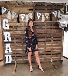 a girl standing in front of a wooden crate with graduation decorations on the wall behind her