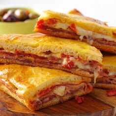 three sandwiches stacked on top of each other with olives in the bowl behind them