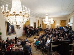 a crowd of people standing in a room with chandelier and paintings on the walls