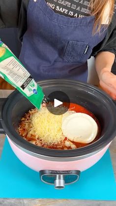 a woman pouring cheese into a crock pot filled with chili and other ingredients to make an enchilada