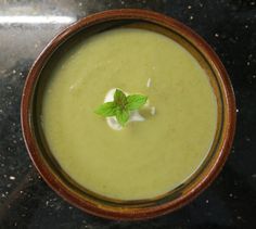 a wooden bowl filled with green soup on top of a black counter next to a white flower