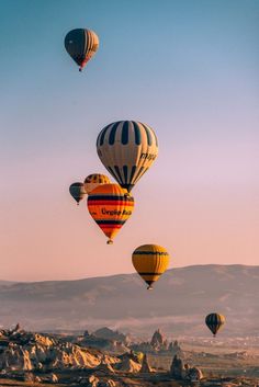 several hot air balloons are flying in the sky over some rocks and mountains on a sunny day