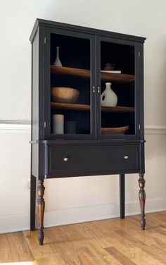 a black cabinet with two glass doors and some vases on it's shelves