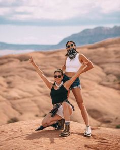 two women posing on top of a rock in the desert with their arms up and legs crossed