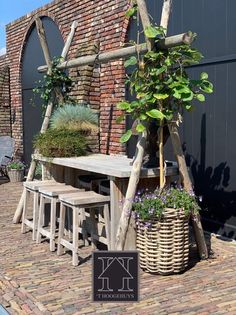 an outdoor table and bench made out of wood sticks with plants growing on them in front of a brick building