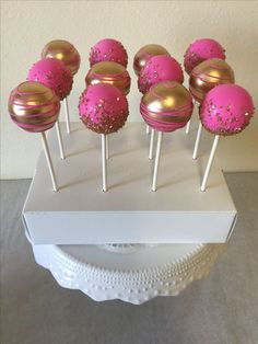 pink and gold cake pops sitting on top of a white box