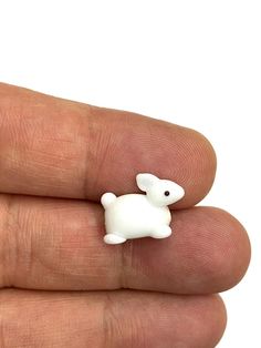 a small white toy animal sitting on top of someone's finger