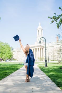 a woman in graduation gown holding up a blue cap and gown while walking down a sidewalk