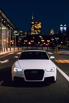 a white car parked on the street in front of a cityscape at night