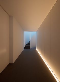 an empty hallway with stairs leading up to the light at the end is lit by white lights