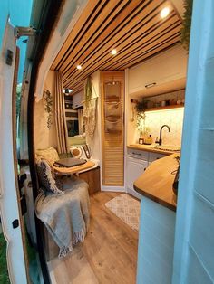 an interior view of a camper van with wood flooring and white walls, showing the kitchen area