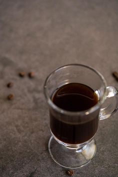 a glass cup filled with liquid sitting on top of a table next to coffee beans