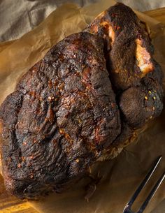 two pieces of meat sitting on top of a wooden cutting board next to a knife and fork