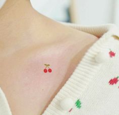 a woman with a cherry tattoo on her chest and back shoulder, wearing a white sweater