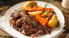 a white plate topped with roast, potatoes and carrots on top of a wooden table