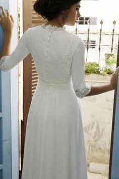 a woman standing in front of a door wearing a white dress and holding her hand out