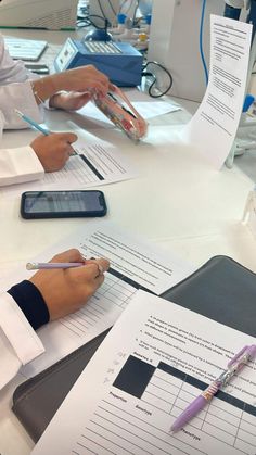 three people sitting at a table with papers and pens in front of them on top of each other