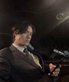 a man in a suit and tie sitting in a car looking at his cell phone