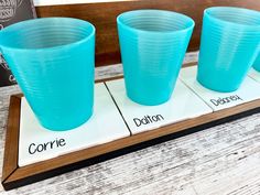 three blue plastic cups sitting on top of a wooden tray next to a sign that says corre