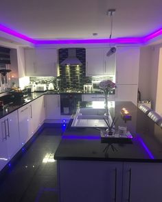 a kitchen with white cabinets and blue lights on the counter tops is lit up at night