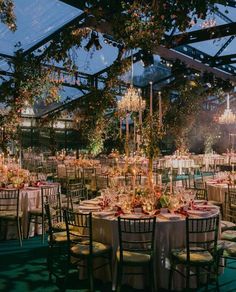 tables and chairs are set up for a formal dinner under a glass roof with chandeliers