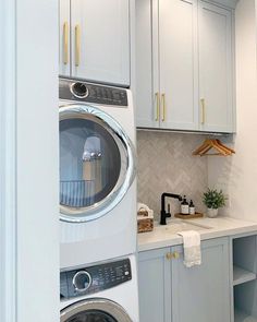 a washer and dryer in a small laundry room with white cabinetry, marble counter tops and gold handles