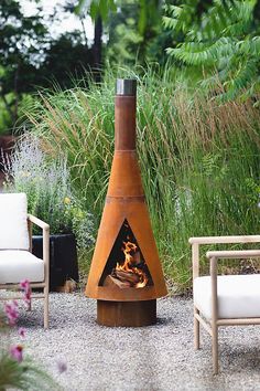 a fire pit sitting in the middle of a gravel area next to chairs and plants