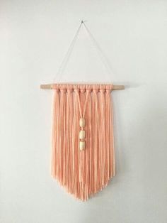 an orange wall hanging with wooden beads and tassels on the end, in front of a white wall