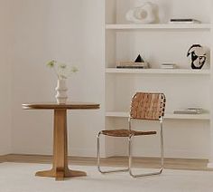 two chairs and a table in a white room with shelves on the wall behind them