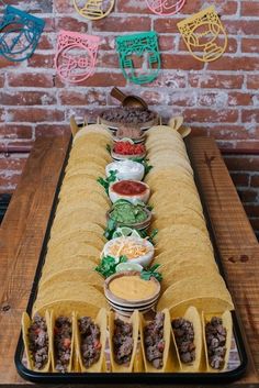 mexican food is lined up on a long serving tray in front of a brick wall