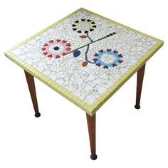 a mosaic table with wooden legs and a flower design on the top, sitting against a white background