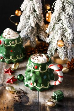 two christmas mugs sitting on top of a table next to trees and candy canes