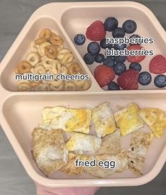 a person holding two trays with different foods in them, including eggs, berries and blueberries