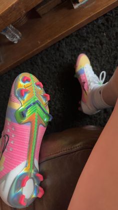 a woman's feet with colorful shoes on the floor next to a brown chair