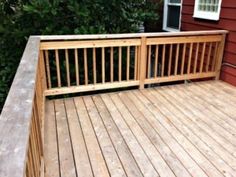 a wooden deck next to a red house with trees and bushes in the back ground